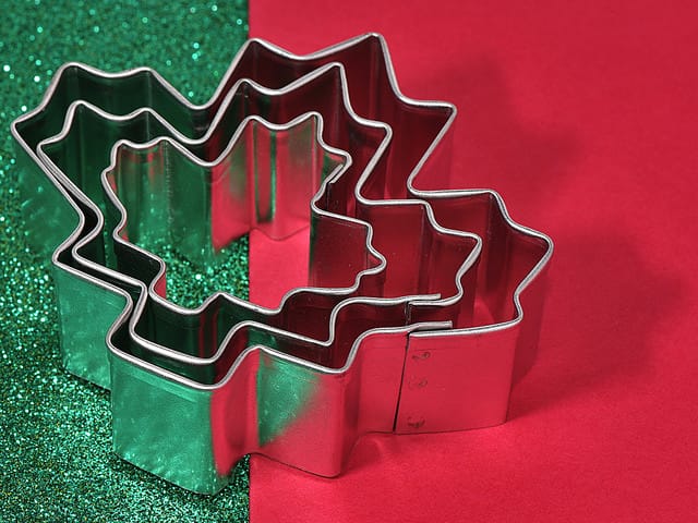 Metal tree-shaped cookie cutters stacked on a red and green glittery background.
