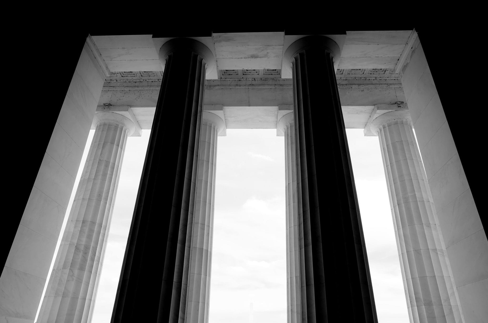 Black and white image of a view through tall, classical columns looking out onto a clear sky.
