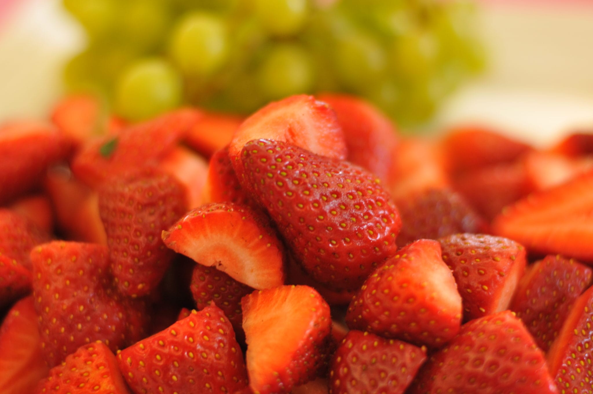 Close-up of freshly sliced strawberries with a bunch of green grapes in the background.