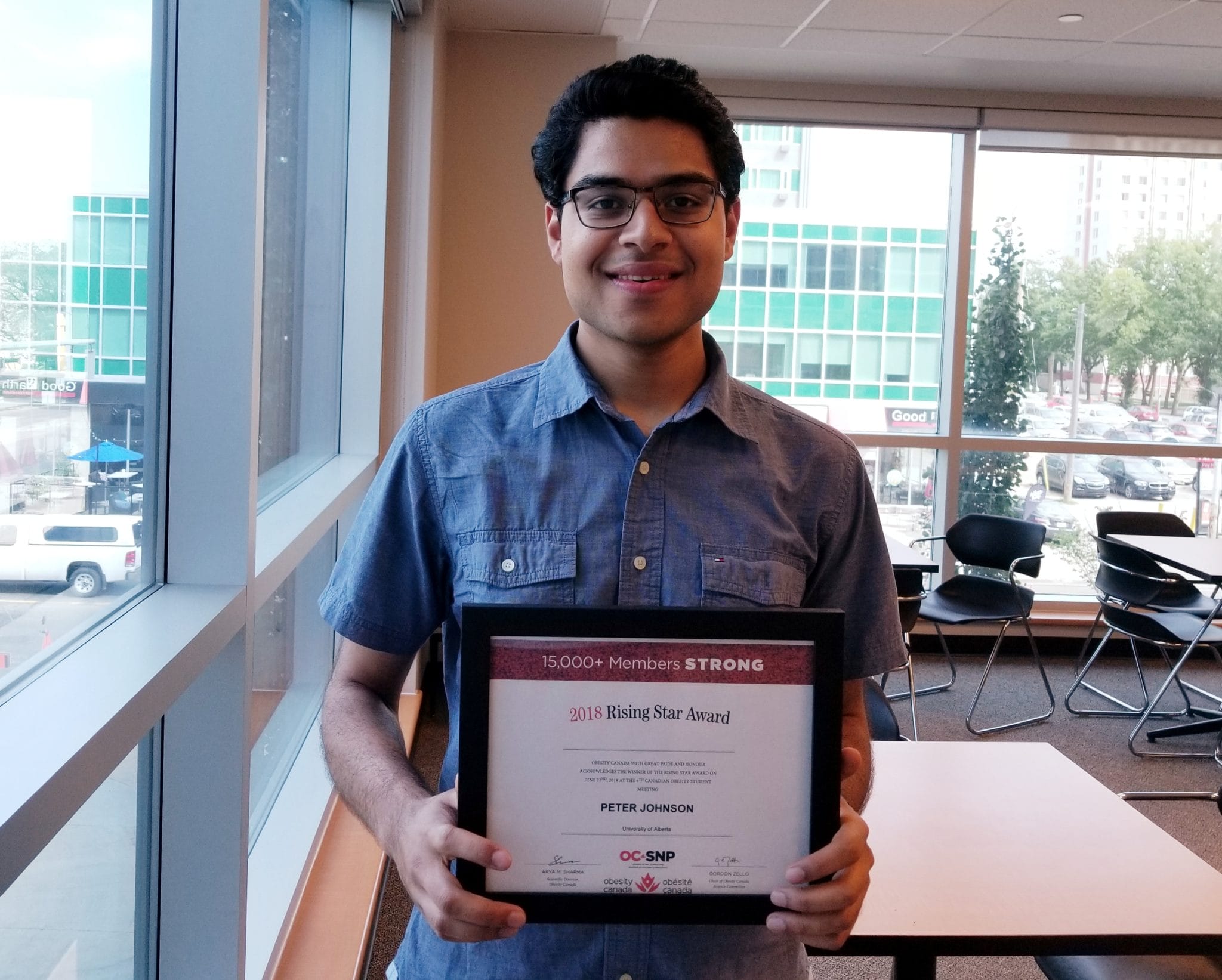A young man holding a "2018 rising star award" certificate inside an office building, smiling at the camera.