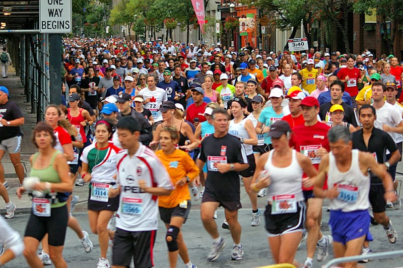 A large group of diverse runners participating in a marathon on a city street, surrounded by buildings and spectators.