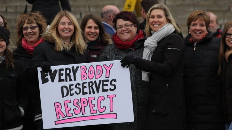 Group of smiling women holding a sign that reads “everybody deserves respect” at an outdoor event.