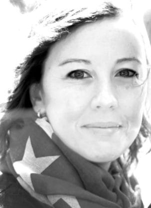 Black and white portrait of a woman smiling gently, wearing a scarf with star patterns, with a bright background.
