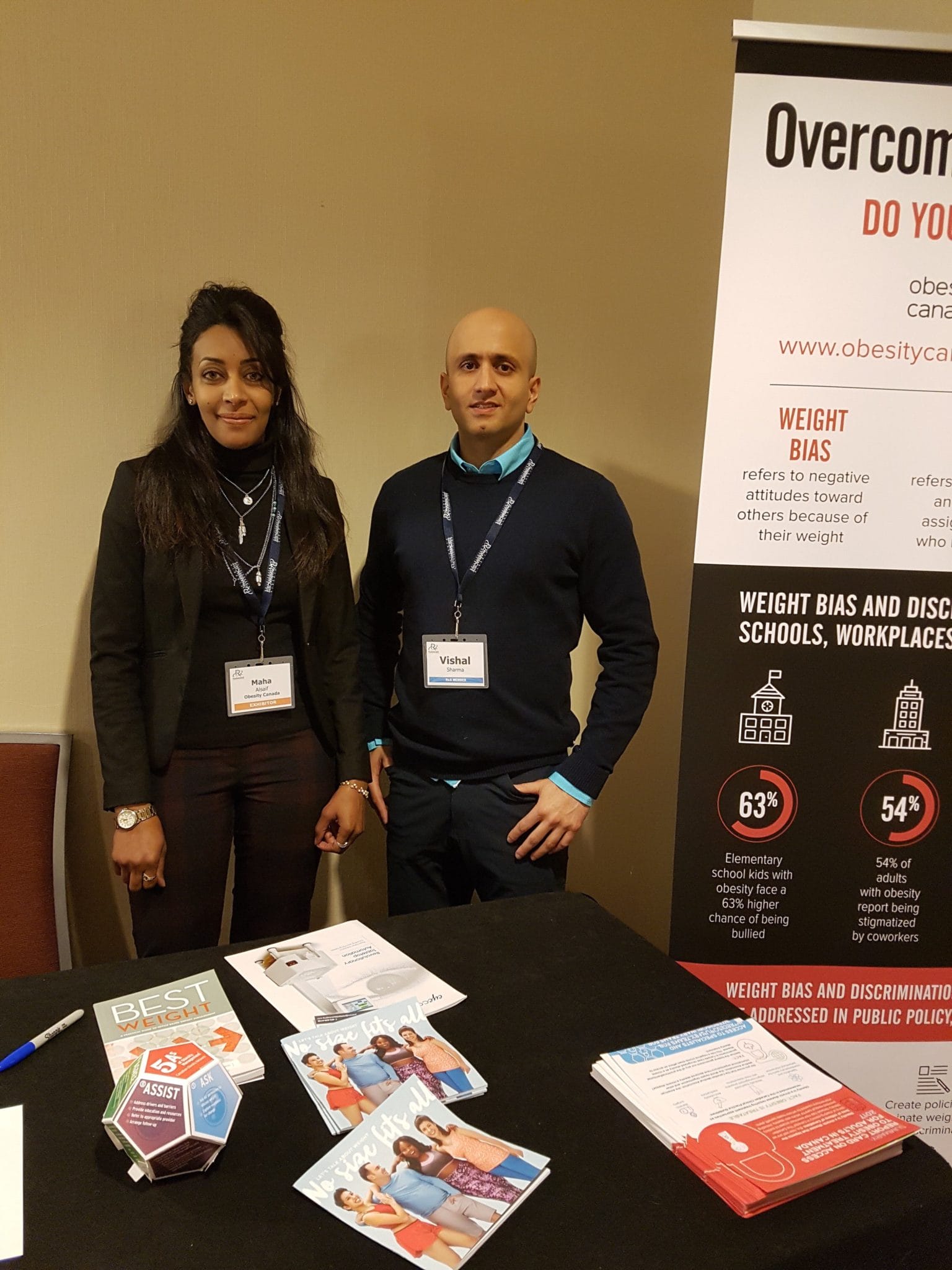 Two people standing at a conference booth with informational materials and banners on weight bias and discrimination.