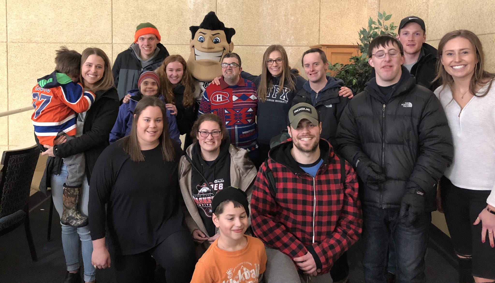 A group of adults and one child posing with a sports mascot indoors, smiling for the camera. some individuals wear various hockey jerseys.