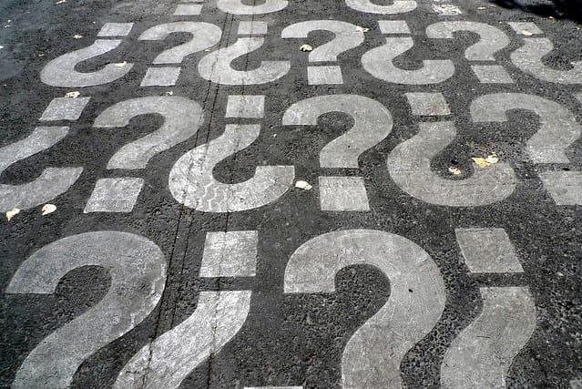 White question marks painted on a black asphalt road, covering the entire visible surface.