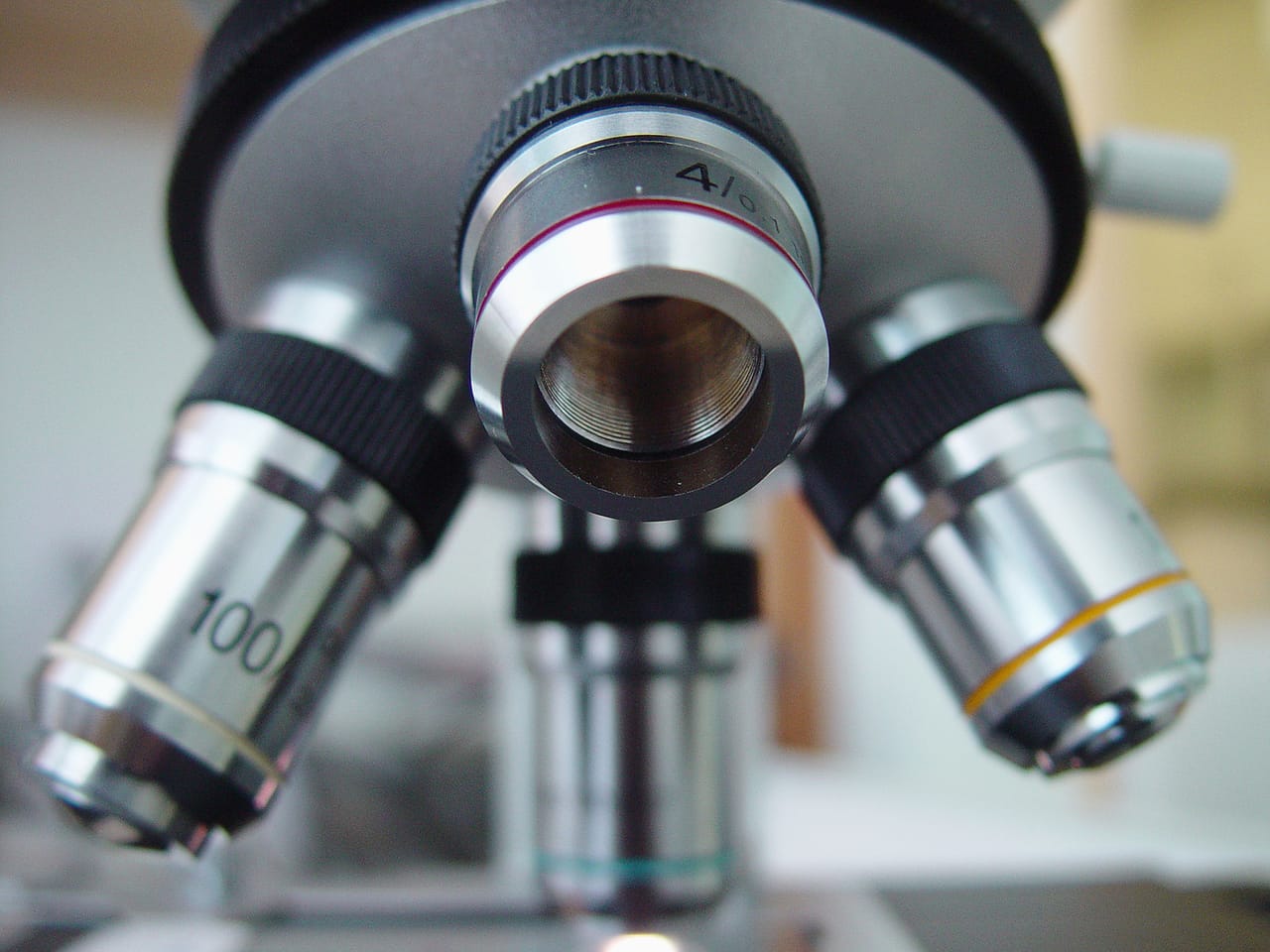 Close-up view of a microscope with three objective lenses labeled 4x, 10x, and 100x, focusing down onto a slide.