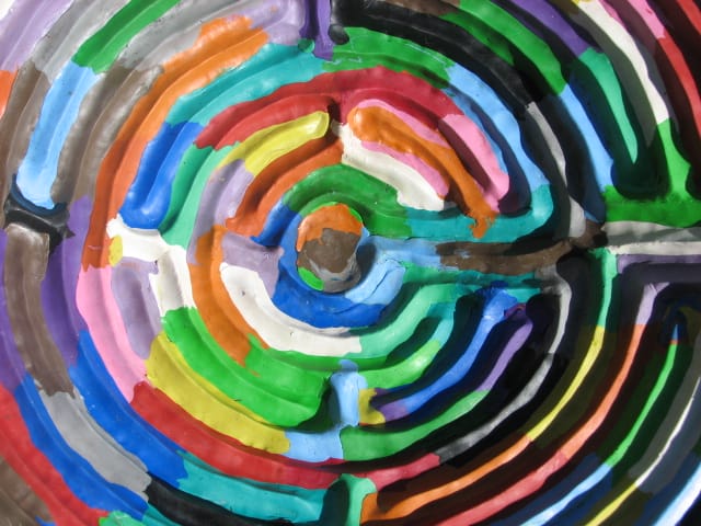 Colorful concentric circles created with thick layers of paint in a rainbow spectrum, displayed in a swirling pattern.