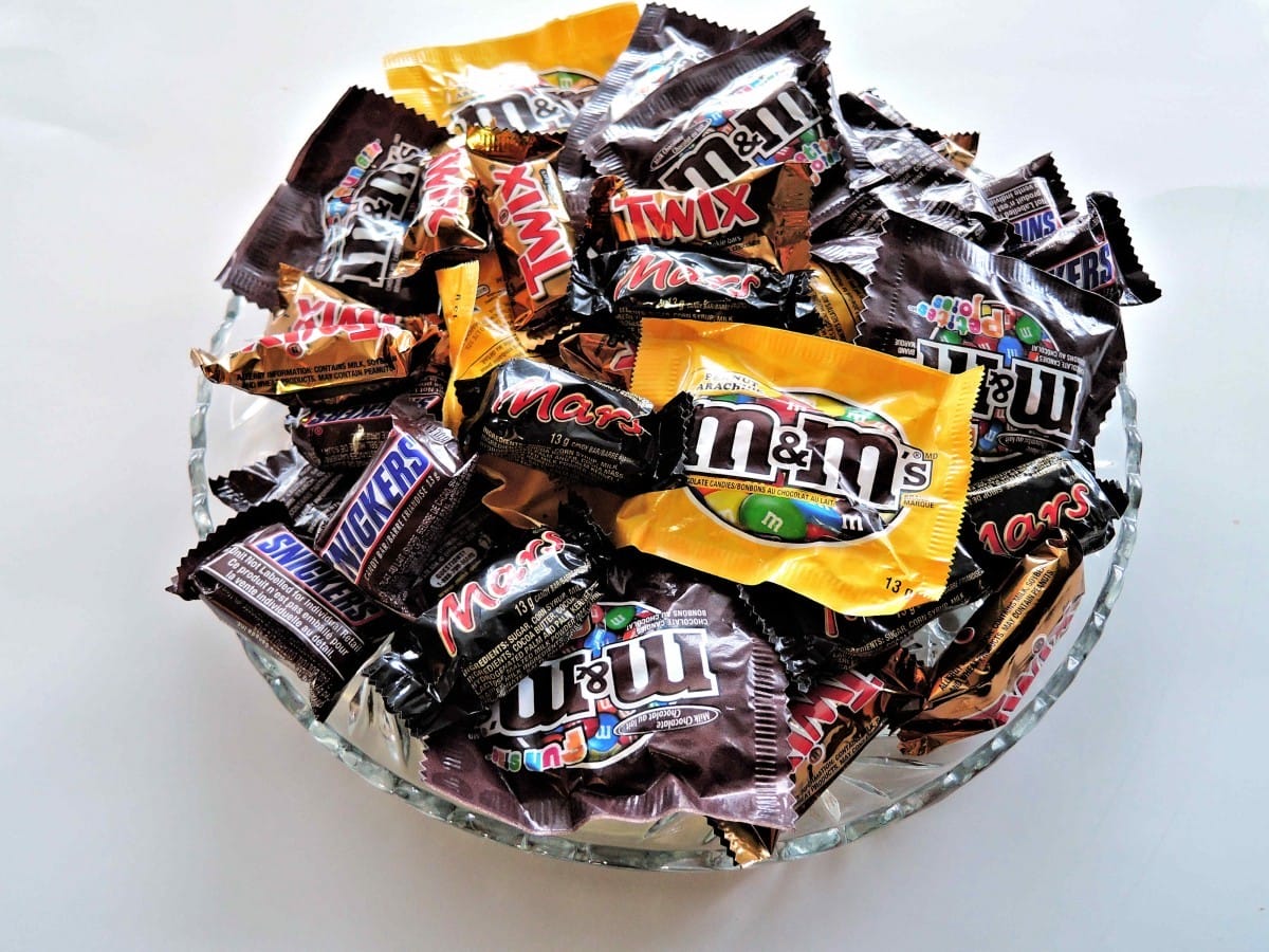 A glass bowl filled with various mini chocolate bars and candy packets, including m&ms, snickers, milky way, and twix.