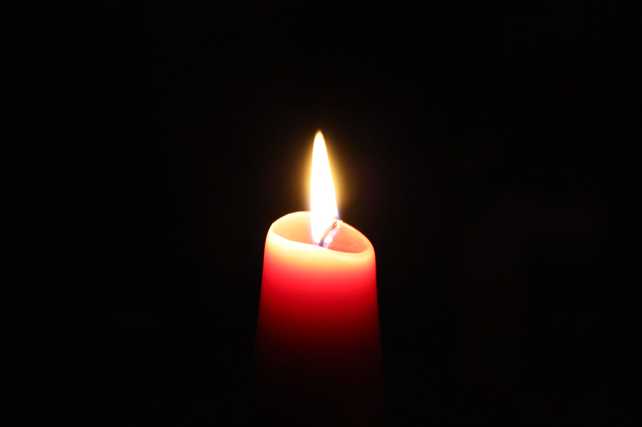 A single red candle burning brightly in a dark room.