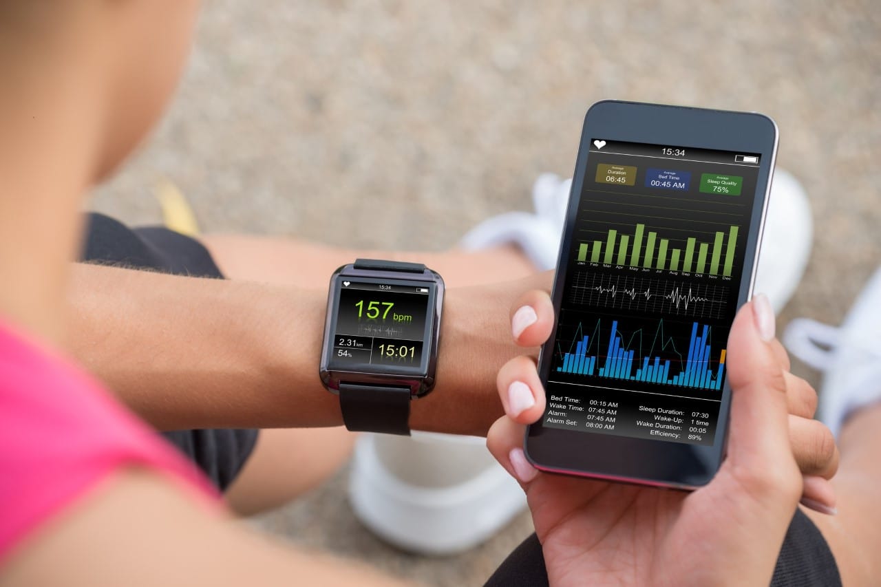 A person checking a fitness tracker on their wrist and comparing it with health stats displayed on a smartphone.
