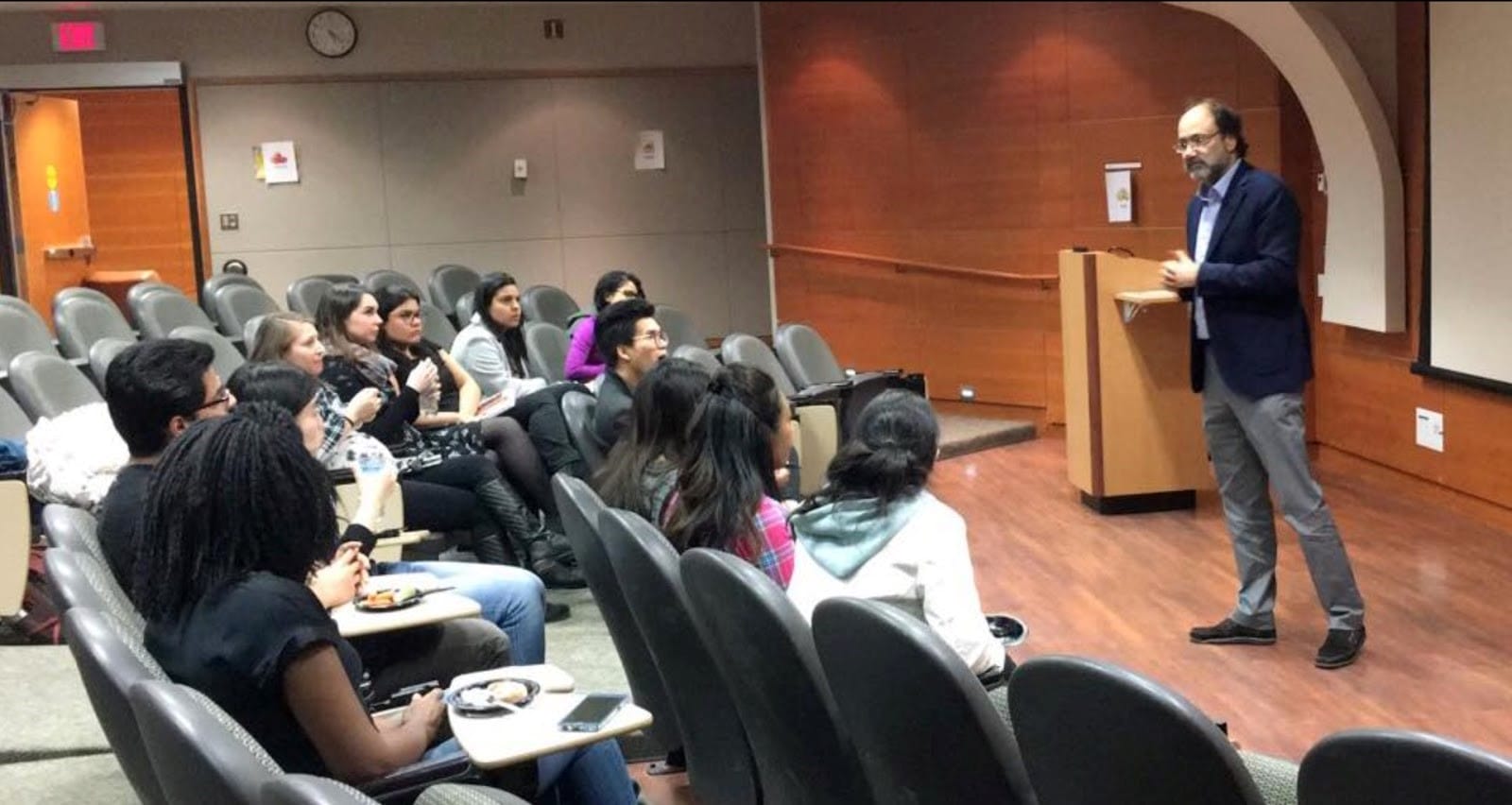 A man lecturing to a diverse group of students in a university classroom.