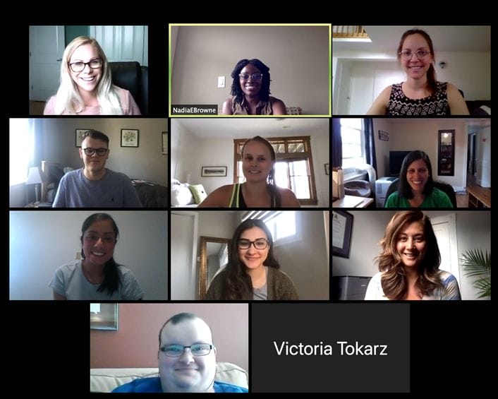 Nine people participating in a virtual meeting, displayed in a grid view with each person smiling from different rooms.