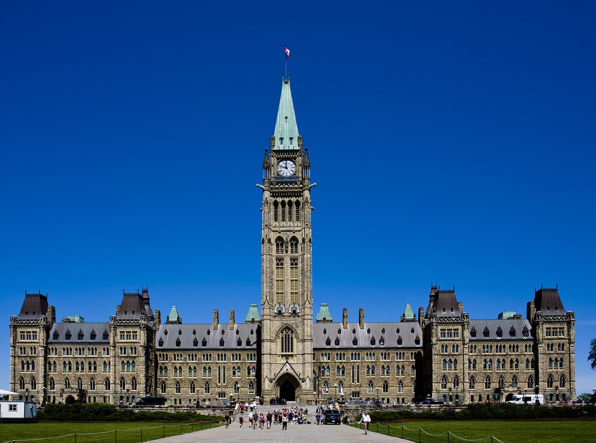The centre block of the parliament buildings in ottawa, canada, with a large clock tower, under a clear blue sky.