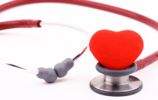 Red stethoscope with a heart-shaped object at its center, lying on a white background.