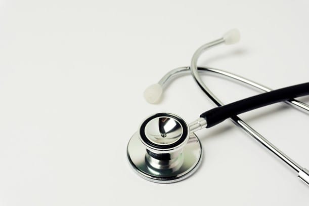 A stethoscope with a shiny silver chest piece and black tubing, lying on a white surface.