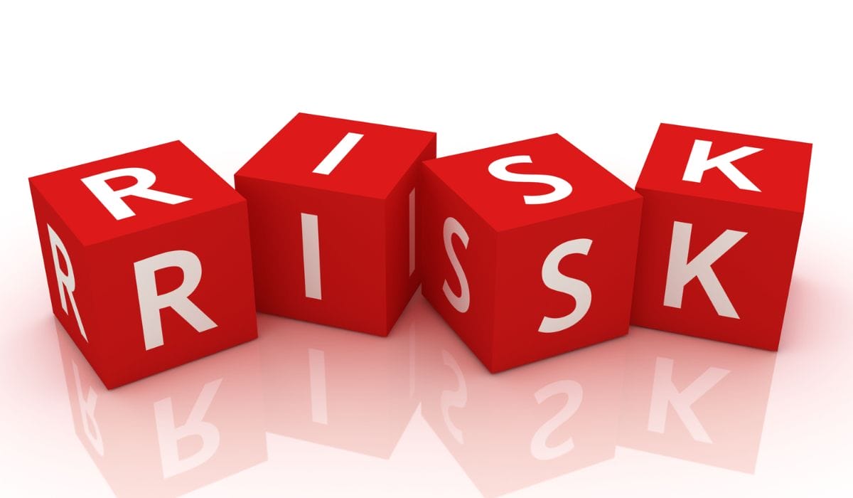Five red cubes with letters that spell out "risk" on a reflective white surface.