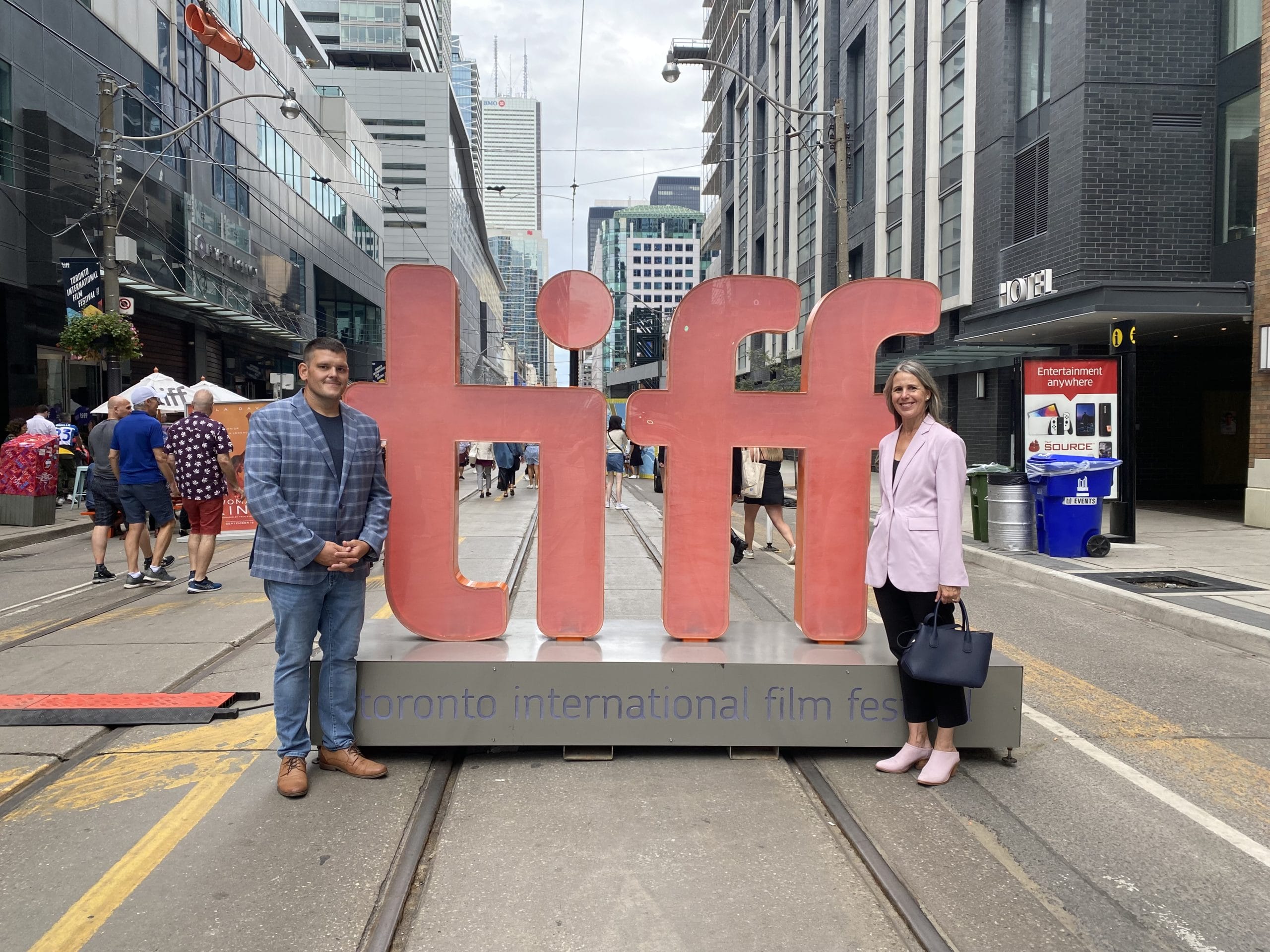 A man and a woman posing next to the large red "tiff" letters at the toronto international film festival on a city street.