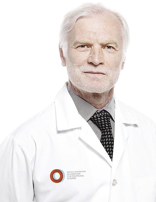 Senior male doctor with white hair and beard, wearing a white lab coat with a badge and a dark tie, standing against a white background.