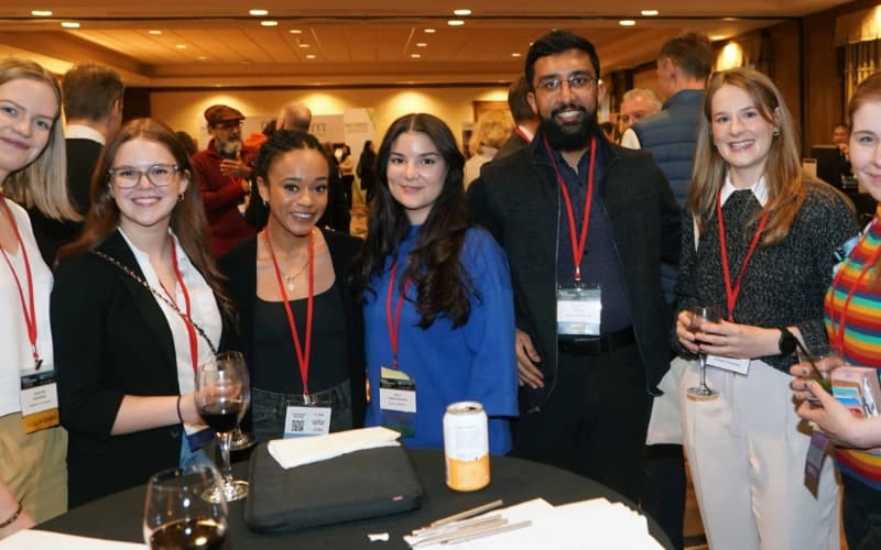 A group of professionals with name tags at a networking event, holding drinks and smiling at the camera.